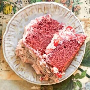 A slice of vegan strawberry came with vegan buttercream frosting and strawberry pieces on a decorative plate. The plate rests on a table with a floral and musical notes design.